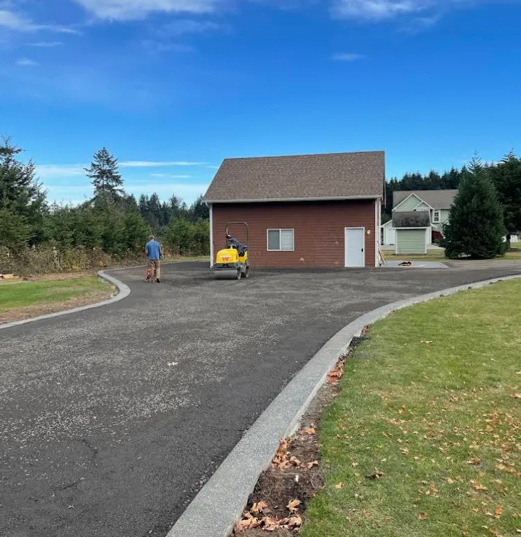 Newly paved asphalt driveway with a concrete curb leading to a garage by Holmes Earth Construction