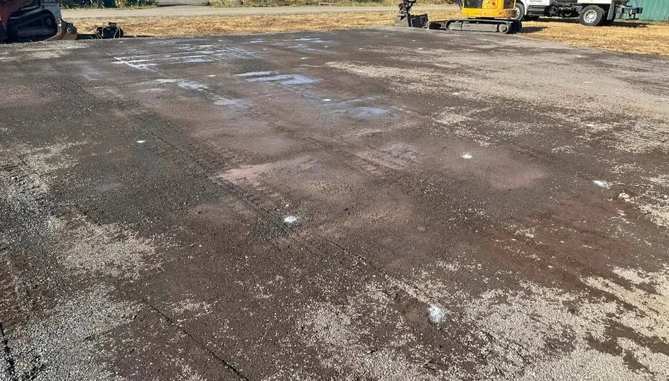 Large compacted gravel pad with an excavator and trucks by Holmes Earth Construction