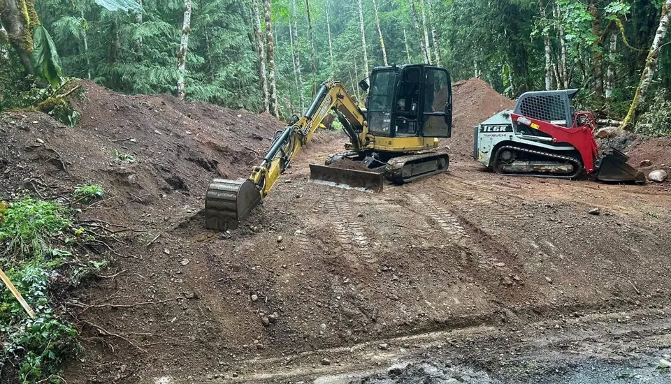 Excavator and track loader cutting a hillside pad in the forest by Holmes Earth Construction